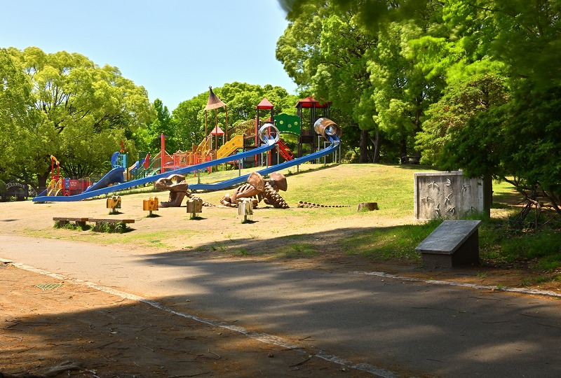 緑に囲まれた平塚市総合公園の遊具広場。カラフルな遊具と恐竜のオブジェがある