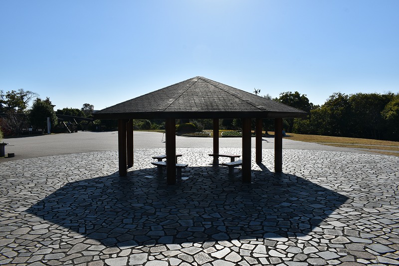 石畳の上に建つ木造の東屋。晴れた日の公園で憩いのスペース